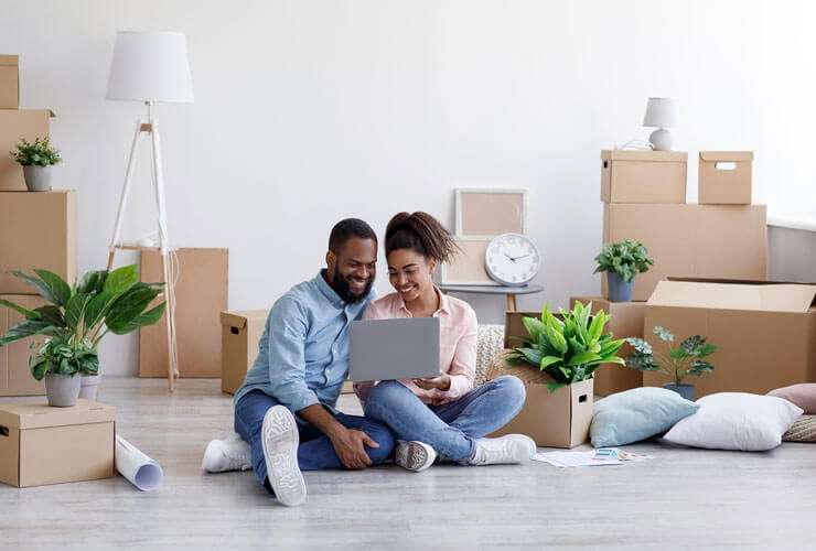 Young mixed race couple sets up internet service on their laptop while surrounded by moving boxes